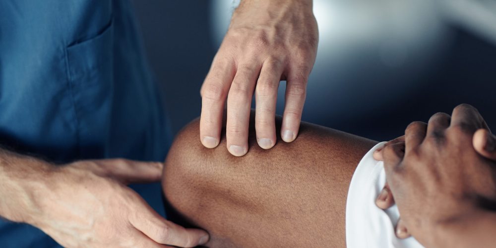 Close-up of doctor examining pain leg of patient during medical exam